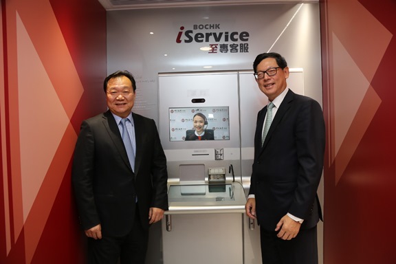 中銀香港副董事長兼總裁岳毅（左）向金管局總裁陳德霖（右）介紹新推出的視像櫃員機服務。