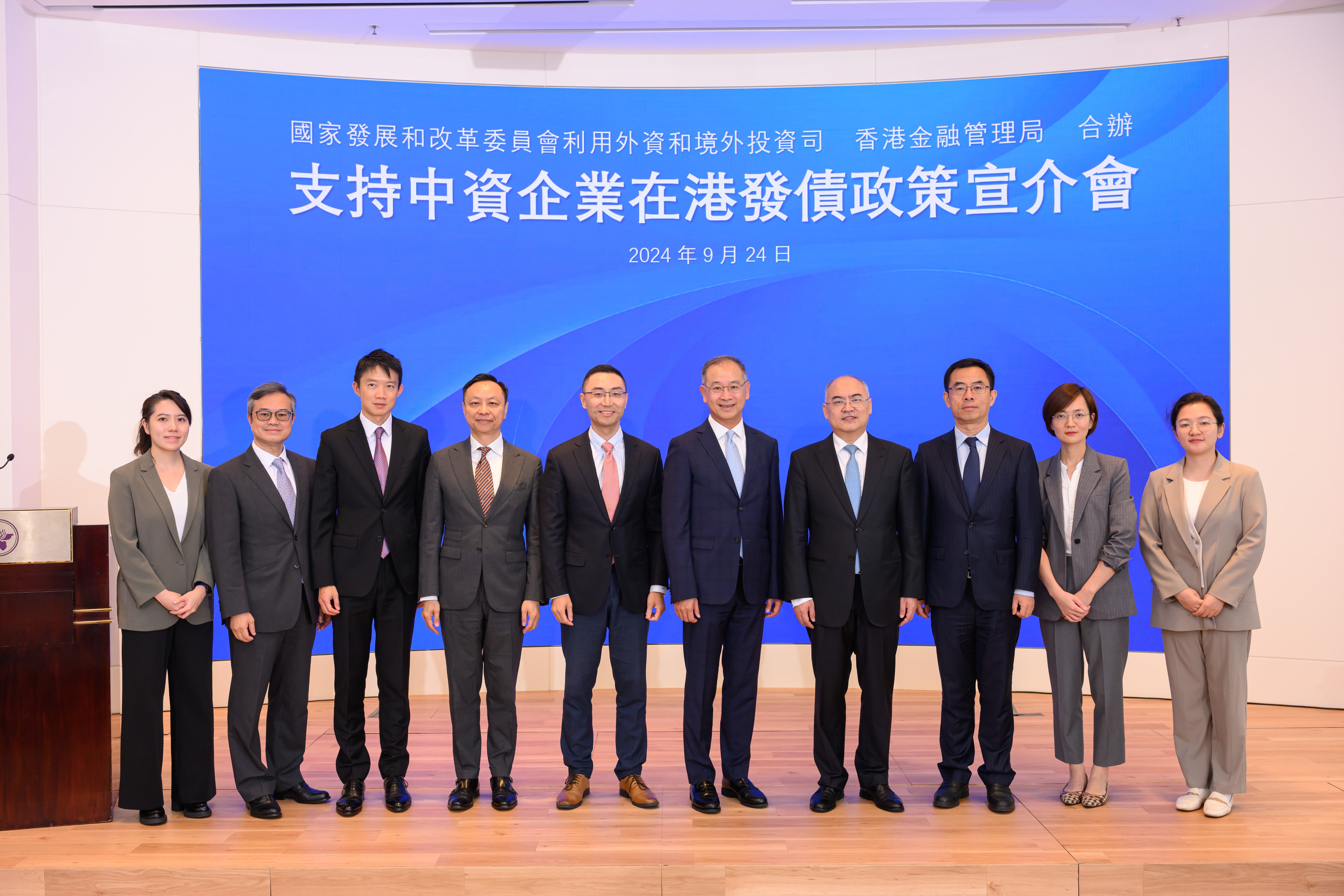國家發展和改革委員會（國家發改委）宣介團、國務院港澳事務辦公室（國務院港澳辦）代表與香港金融管理局（金管局）代表合照。右起為國務院港澳辦三局一級主任科員劉博、重慶市發展和改革委員會區域合作處副處長劉彥儀、國務院港澳辦三局副局長劉承鋼、國家發改委利用外資和境外投資司（外資司）司長鄭持平、金管局總裁余偉文、國家發改委外資司國外貸款處處長竺瑋、金管局副總裁陳維民、金管局助理總裁（外事）許懷志、金管局債務工具中央結算系統總裁陳達強和金管局主管（市場發展）駱家珍。