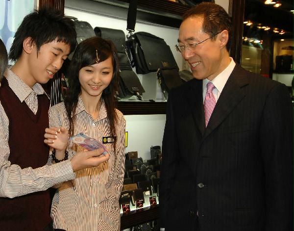 唐英年向鲤鱼门广场内一间皮具店的店员介绍新香港拾元塑质钞票。