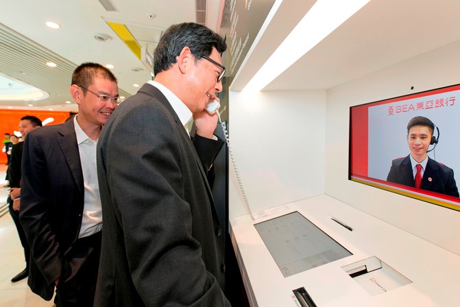 东亚银行执行董事兼副行政总裁李民桥先生（左）向金管局总裁陈德霖先生（右）介绍视像柜员机。